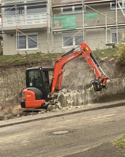 Bagger bricht eine Betonwand mit hydraulischem Abbruchhammer bei Abbrucharbeiten von STROHGÄU GaLaBau im Raum Stuttgart.