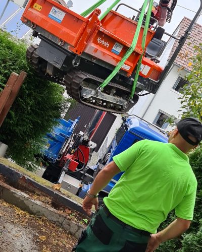 Baumaschine wird mit einem Kran für Arbeiten von STROHGÄU GaLaBau im Raum Stuttgart transportiert.