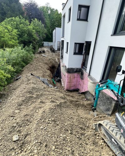 Ausgegrabener Kanal entlang einer Hauswand mit Baggerarbeiten von STROHGÄU GaLaBau im Raum Stuttgart.